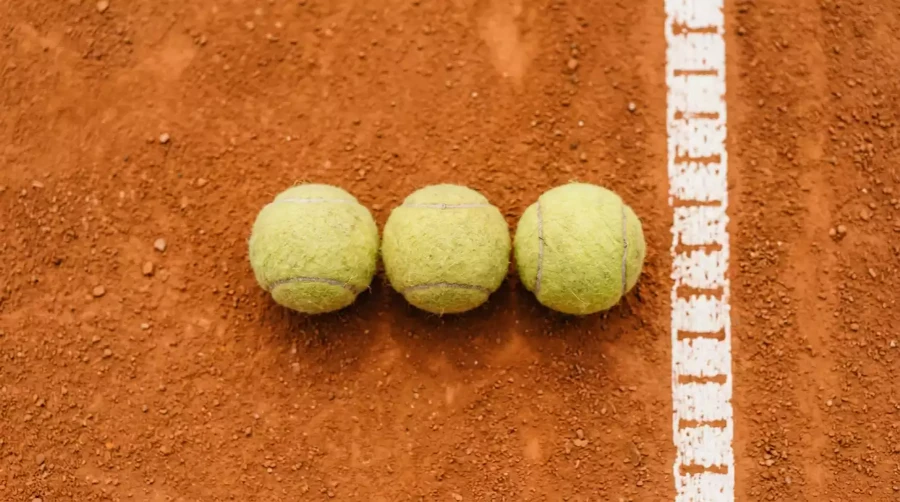 Tres bolas de tenis alineadas sobre pista de tierra batida naranja, representando la selección múltiple en apuestas combinadas de tenis ATP WTA